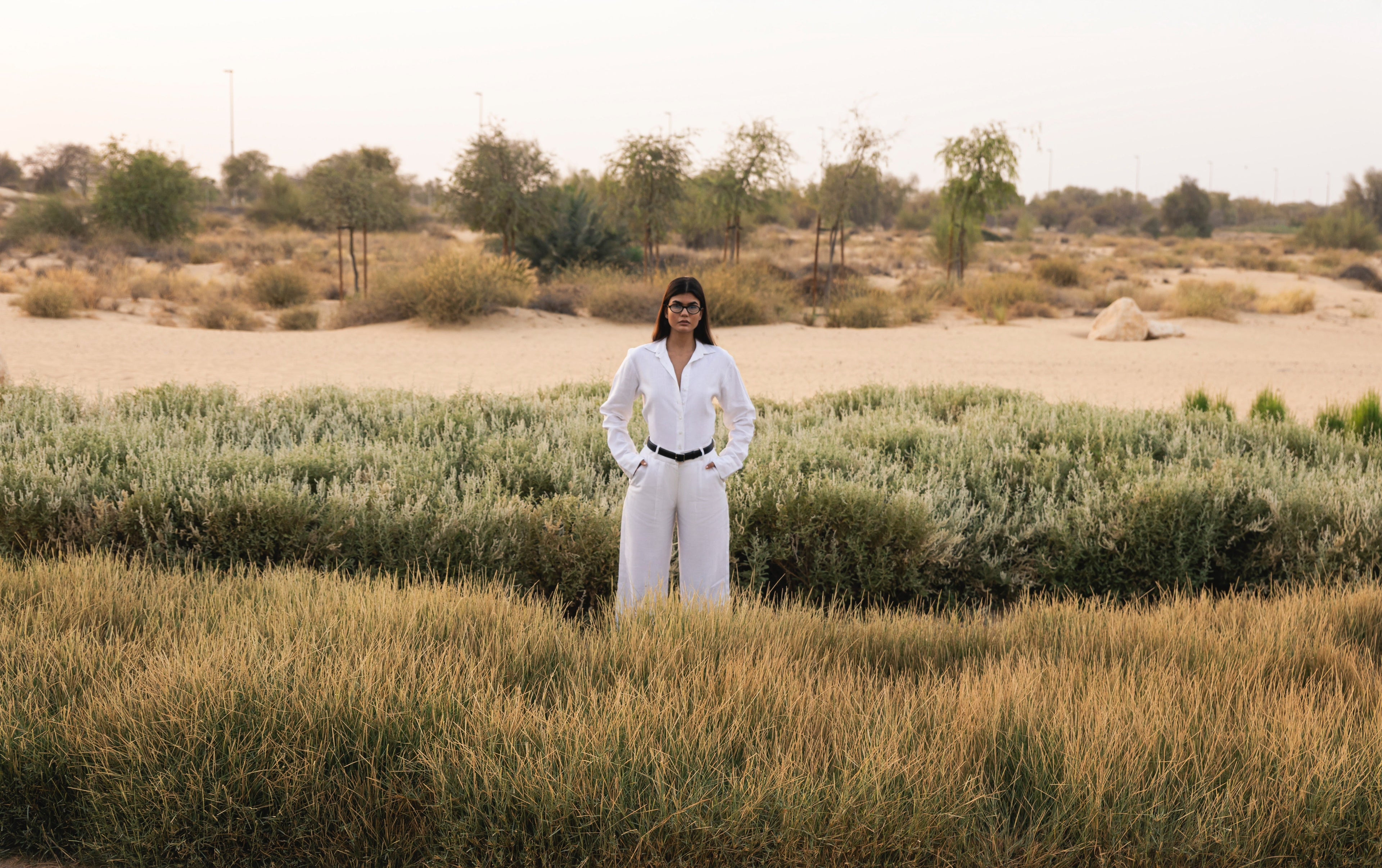 Person in a white outfit standing in a desert landscape with sparse vegetation.
